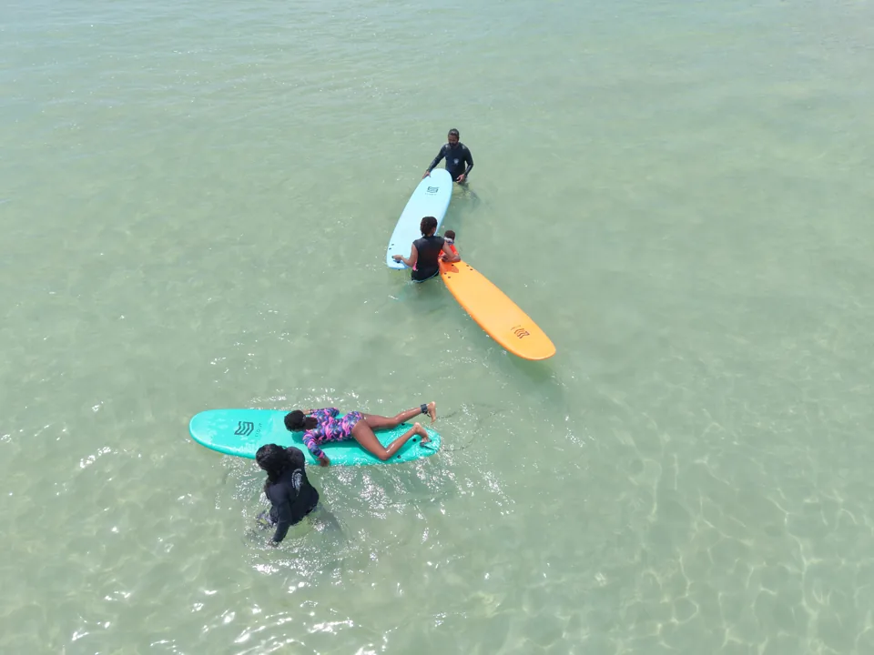 An instructor guides a surfer in the clear water at Kabalana